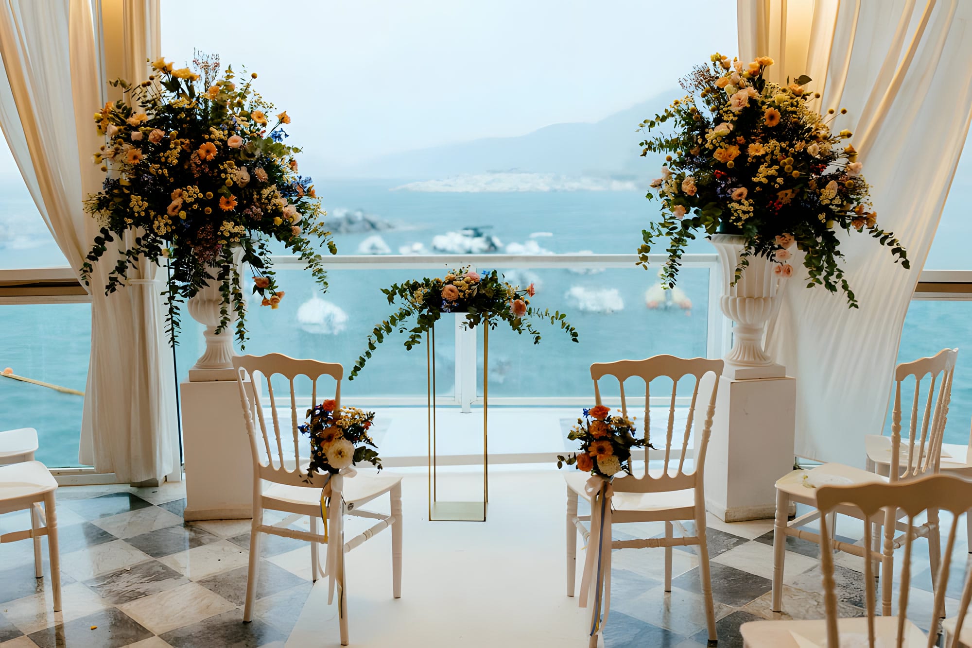 Arco della cerimonia con alte alzate di fiori arancio e pesca, il golfo alle spalle