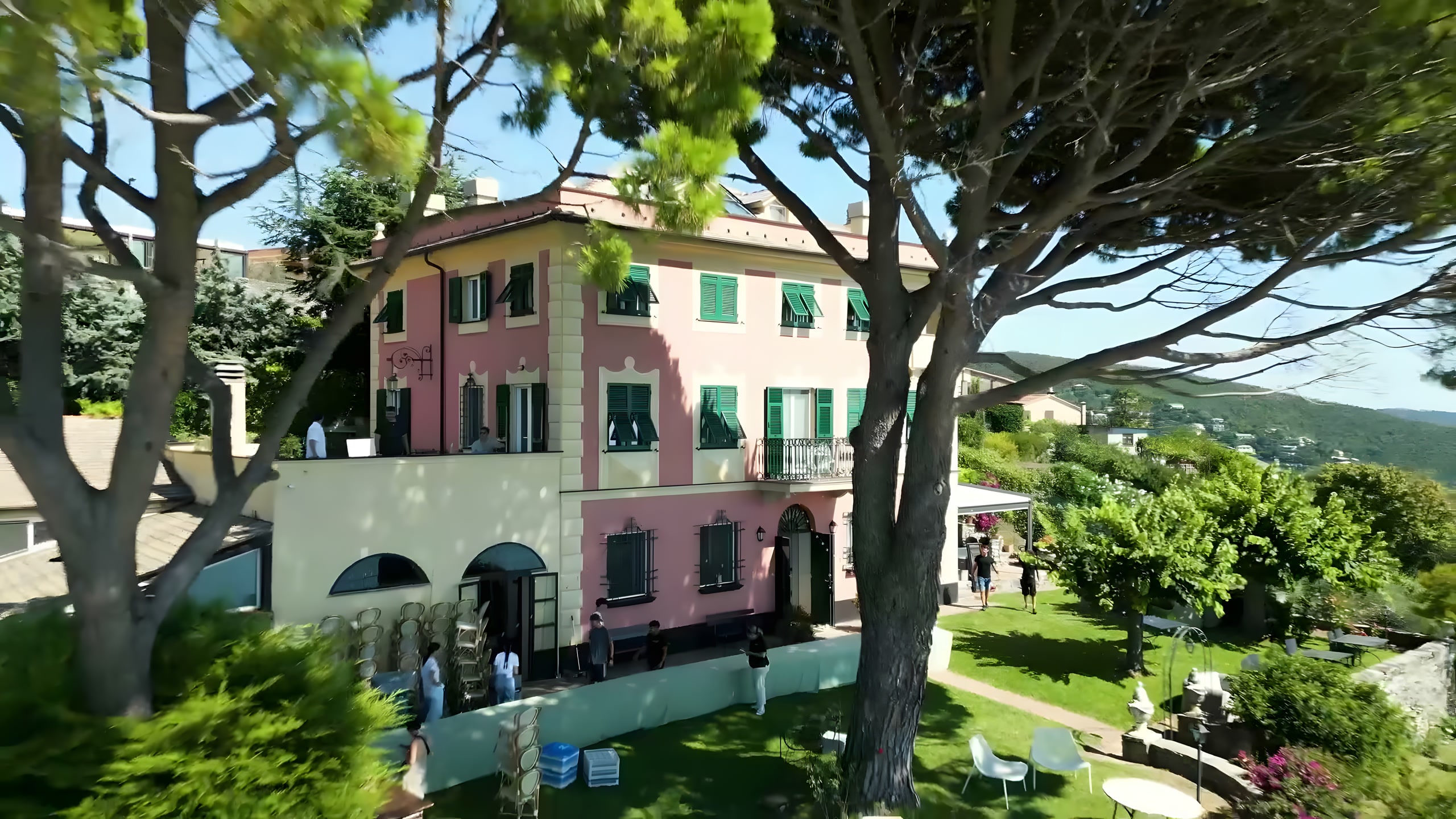 Ripresa aerea di una villa ligure rosa con le persiane verdi, allestita in giardino per un matrimonio